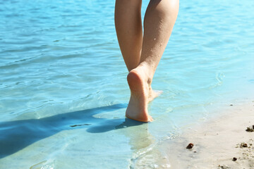 Woman walking barefoot through water on riverbank, closeup