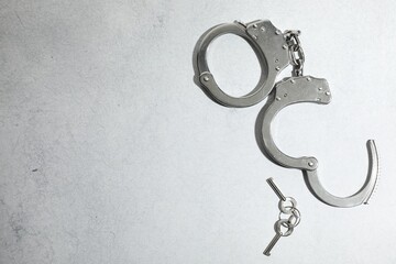 Metal chain handcuffs and keys on light grey table, top view. Space for text