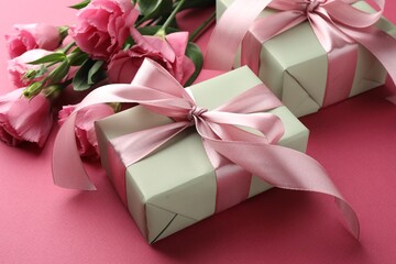 Beautiful gift boxes with bows and eustoma flowers on pink background, closeup