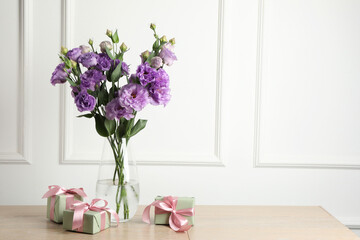 Vase with beautiful eustoma flowers and gift boxes on wooden table, space for text