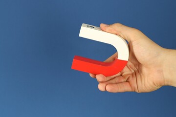 Man holding horseshoe magnet on blue background, closeup. Space for text