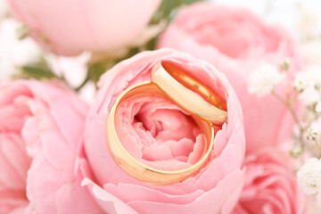 Golden wedding rings and flowers on blurred background, closeup