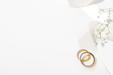 Golden wedding rings, ribbon and flowers on white background, above view. Space for text