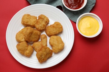Delicious chicken nuggets and sauces on red background, flat lay