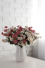 Vase with beautiful flowers on wooden table near white brick wall