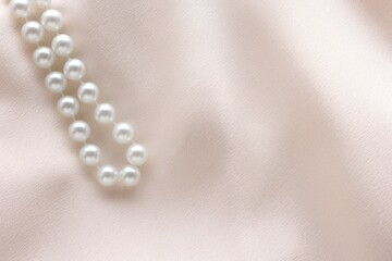 Beautiful pearl necklace on beige cloth, top view. Space for text