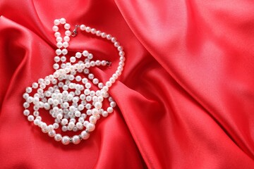 Beautiful bijouterie with pearls on red cloth, top view. Space for text
