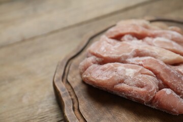 Frozen pieces of chicken fillet on wooden table, closeup. Space for text