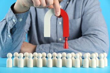 Man with magnet attracting red piece among wooden ones on light blue background, closeup