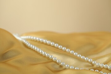 Beautiful pearl necklace on golden silk, closeup. Space for text