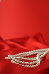 Obraz premium Beautiful pearl necklace on red silk, closeup. Space for text