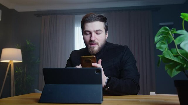 A businessman holds up a stack of cash and mobile phone while speaking to the camera in a professional home office. Investment, cryptocurrency, and wealth management