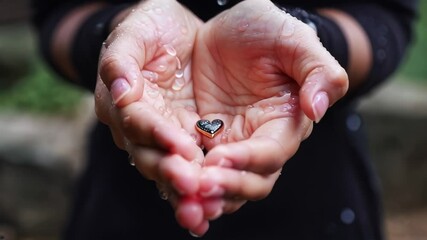 Hands holding a small heart-shaped pendant with water droplets, symbolizing love, care, and vulnerability, ideal for emotional and inspirational themes, conveying connection and warmth