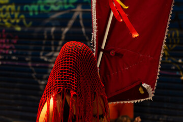 Mulher com véu vermelho na cabeça carregando um estandarte em um bloco de carnaval de rua. 