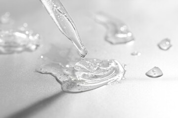 Dripping cosmetic serum from pipette on grey background, closeup