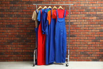 Different workers' uniforms on clothing rack near brick wall