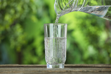 Pouring soda water in glass at wooden table outdoors