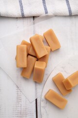 Tasty sweet caramel candies on white wooden table, flat lay
