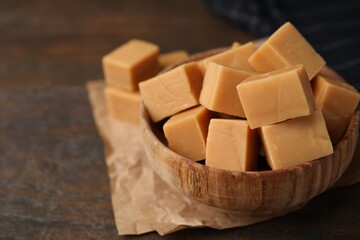 Tasty sweet caramel candies in bowl on wooden table, closeup. Space for text