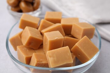 Tasty sweet caramel candies in bowl on light table, closeup