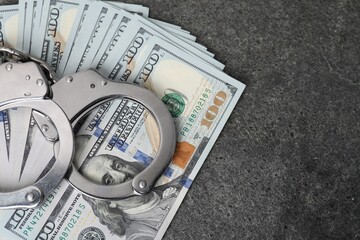 Corruption concept. Handcuffs and dollar banknotes on grey table, top view. Space for text