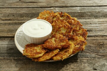 Delicious potato pancakes and sour cream on wooden table, closeup