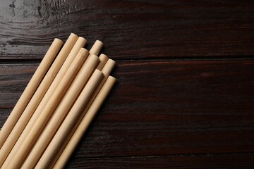 Bamboo drinking straws on wooden table, top view. Space for text