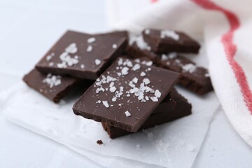 Pieces of chocolate with salt on white table, closeup