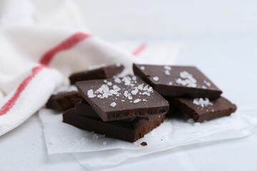 Pieces of chocolate with salt on white table, closeup