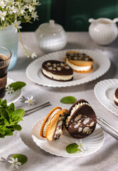 Delicious homemade cookies with cream filling, almonds and chocolate decorated with mint leaves on table