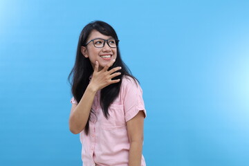 Cheerful Asian female gazes aside daydreams and remembers lovely moment smiles expresses positive candid emotions isolated blue background. Youth lifestyle