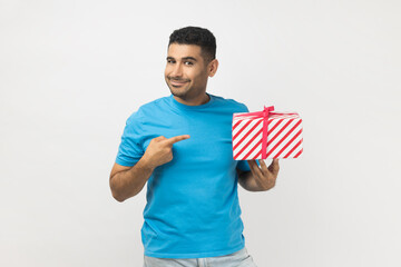 Smiling unshaven man pointing at wrapped present box, looking at camera, congratulating.