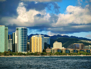 Vibrant skyline of Honolulu with modern skyscrapers and lush mountains under a dramatic sky during the late afternoon