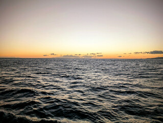A tranquil sunset over the calm ocean, with gentle waves reflecting warm colors on the water in a serene evening atmosphere