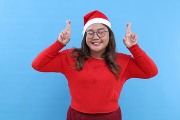 Excited young Asian woman with santa hat keeps fingers crossed for Christmas wish