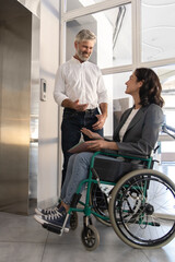 Man with disabled colleague standing at the elevator for inclusion