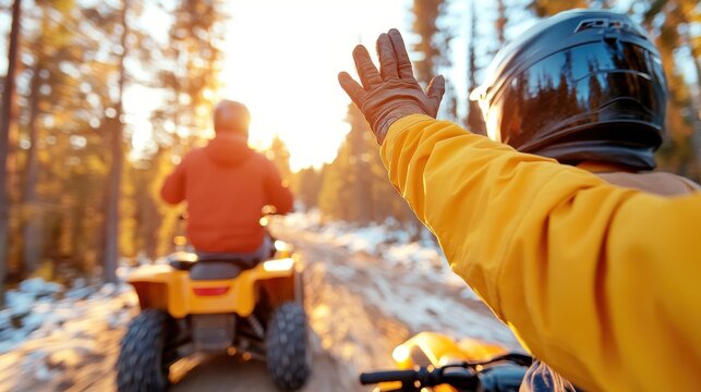 Riders on ATVs wave at one another, capturing the spirit of adventure and camaraderie, as they drive through a sunlit forest path wearing protective gear.