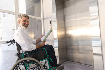Businessman in wheelchair reviews documents while waiting for lift in office building