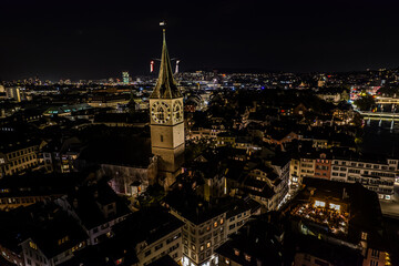 Fototapeta premium Beautiful aerial view of the city of Zurich in Switzerland at night - the Limmat River and its iconic churches, buildings rivers and Clocks.