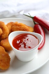 Chili sauce and chicken nuggets on white table, closeup