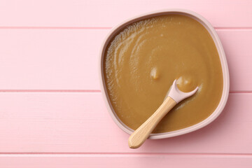 Delicious baby food and spoon in bowl on pink wooden table, top view. Space for text