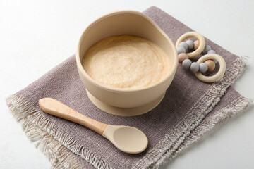Delicious baby food in bowl with spoon and teether on white background
