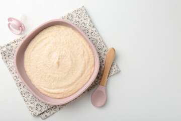 Delicious baby food in bowl with spoon and pacifier on white background, top view. Space for text