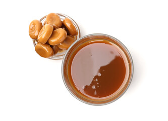 Tasty caramel sauce in glass bowl and candies isolated on white, top view