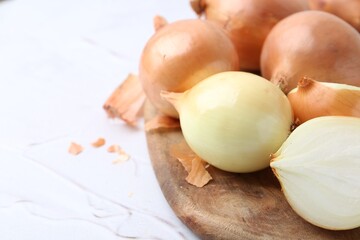 Fresh onions with peels on light textured table, closeup. Space for text