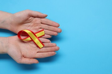 Woman with yellow and red ribbon on light blue background, top view with space for text. Hepatitis C awareness