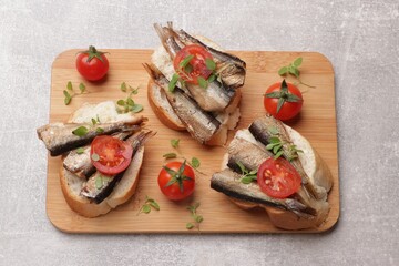 Delicious sandwiches with sprats, microgreens and tomatoes on grey table, top view