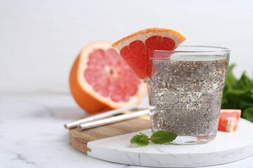 Glass of drink with chia seeds and grapefruit on white marble table, closeup