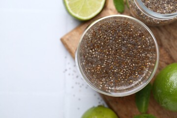 Glass of drink with chia seeds and lime on white tiled table, flat lay. Space for text