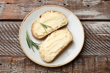 Fresh bread with butter and rosemary on wooden table, top view